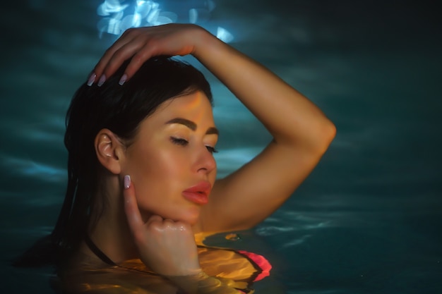Portret brunetki pływa w basenie z wodą geotermalną w spa, kurorty z gorącymi źródłami o zmierzchu