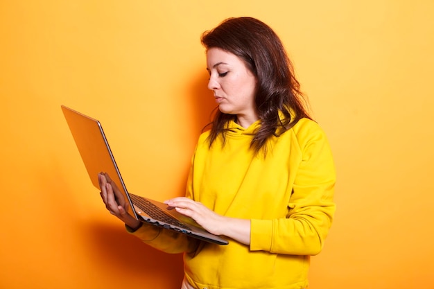 Portret brunetki trzymającej komputer bezprzewodowy w studiu nad izolowanym tłem Kaukazyjka nosząca i używająca swojego cyfrowego laptopa do badań online