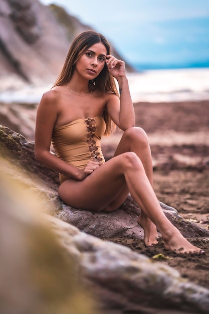 Portret brunetki w stroju kąpielowym na plaży latem siedzącej na skałach