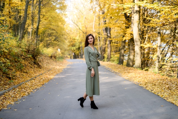 Portret brunetki w zielonej sukience pozuje w jesiennym parku