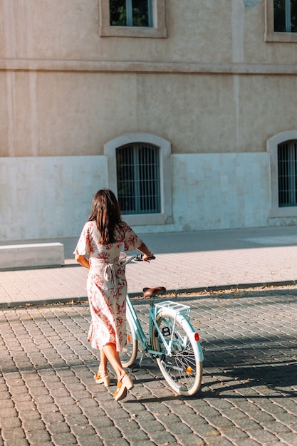 Portret całego ciała pięknej stylowej kobiety ubranej w płaszcz stojącej z retro rowerem na zewnątrz