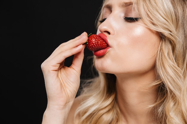 Portret całkiem młoda blond kobieta z jasny makijaż czerwone usta pozowanie na białym tle jeść truskawki.