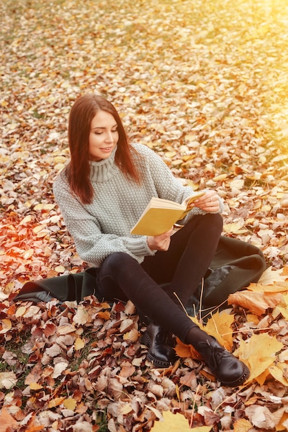 Portret całkiem młoda kobieta o słowiańskim wyglądzie w odzieży casual jesienią, czytanie książki na polanie. Ładny model spaceru w parku w złotej jesieni na tle przyrody. Skopiuj miejsce