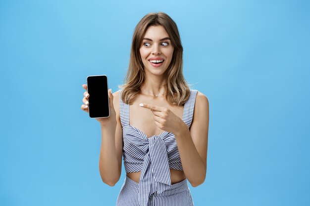 Portret charyzmatycznej, zdumionej i szczęśliwej kobiety z uroczymi rozwartymi zębami, uśmiechnięta podekscytowana i zaskoczona, trzymając niesamowity smartfon wskazujący na ekran urządzenia i patrząc na gadżet zdziwiony i zachwycony