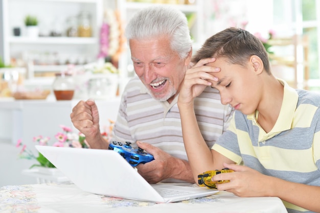 Portret chłopca i dziadka grających w grę komputerową z laptopem w domu