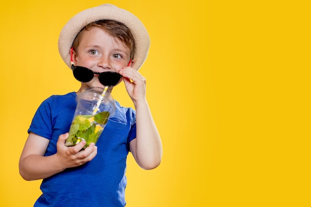 Portret chłopca nosi okulary przeciwsłoneczne i pije lemoniadę w plastikowym kubku