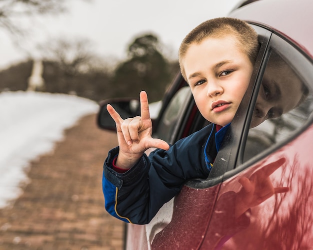 Portret chłopca pokazującego znak rogu przez okno samochodu na drodze