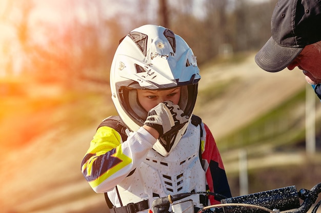 Portret chłopca ubranego i wyposażonego do wyścigów motocyklowych siedzącego na motocyklu