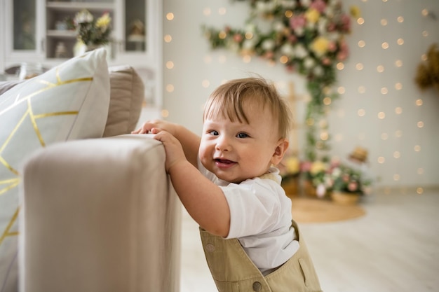 Zdjęcie portret chłopca w beżowym kombinezonie stoi obok sofy w pokoju