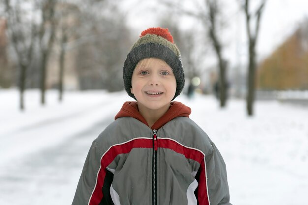 Portret chłopca w ciepłej kurtce i kapeluszu na tle zaśnieżonego parku.