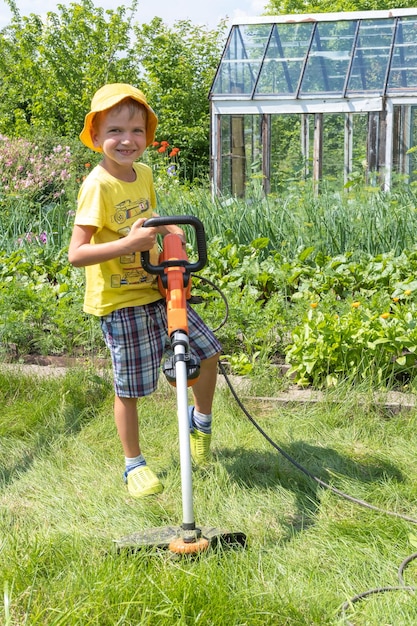 Portret chłopca z elektryczną kosiarką koszącą trawnik Piękno chłopca przycinanie i kształtowanie krajobrazu