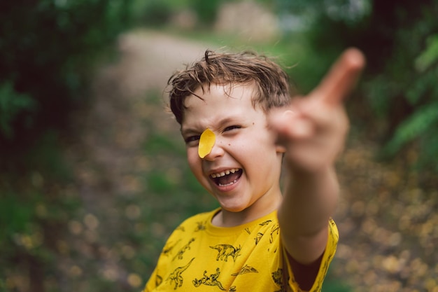 Portret chłopca z żółtym liściem na nosie Szczęśliwe dziecko chłopiec śmieje się i bawi w jesienny dzień Dziecko bawi się liśćmi Jesienny nastrój