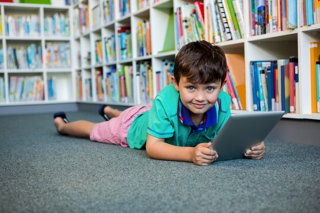 Portret chłopiec używa cyfrową pastylkę w szkolnej bibliotece