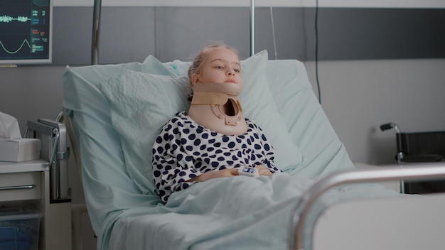 Zdjęcie portret chorego dziecka pacjenta leżącego w łóżku, patrząc na kamerę, mając szyję kołnierza szyjnego dochodzącą do siebie po bolesnej operacji medycyny na oddziale szpitalnym. dziecko noszące rurkę nosową podczas badania
