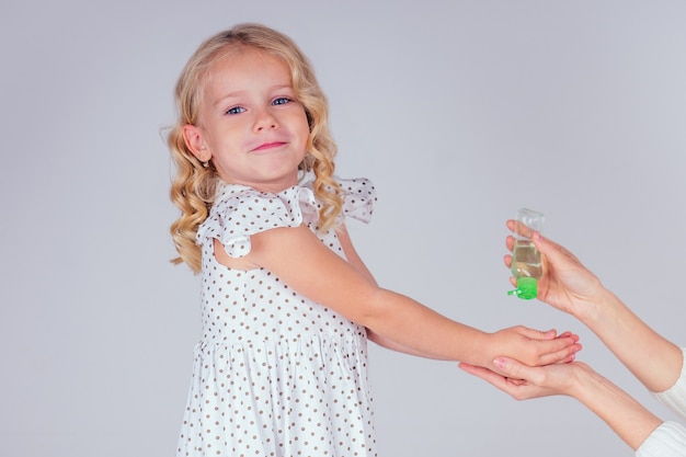 Portret cute little girl blondynka stosując antybakteryjny żel antyseptyczny na ręce anty bakterie wirusy w studio na białym tle. ochrona przed epidemią dziecka, zbliżenie ręki matki.