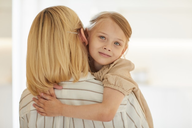 Portret Cute Little Girl Obejmując Szczęśliwą Matkę Z Miłością, Siedząc W Jej Ramionach, Uśmiechając Się