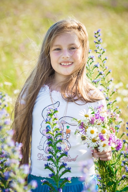 Portret cute little szczęśliwa siedmioletnia dziewczynka z kwiatami łubin kwiatami w polu w naturze na świeżym powietrzu.