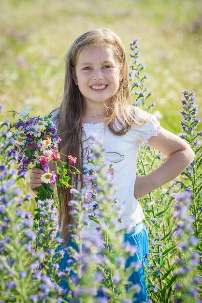 Portret cute little szczęśliwa siedmioletnia dziewczynka z kwiatami łubin kwiatami w polu w naturze na świeżym powietrzu.