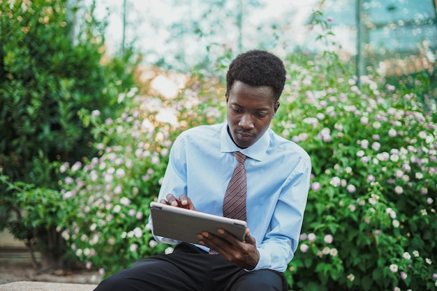 Portret czarnoskórego biznesmena przy użyciu komputera typu tablet, gdy siedzi na ławce