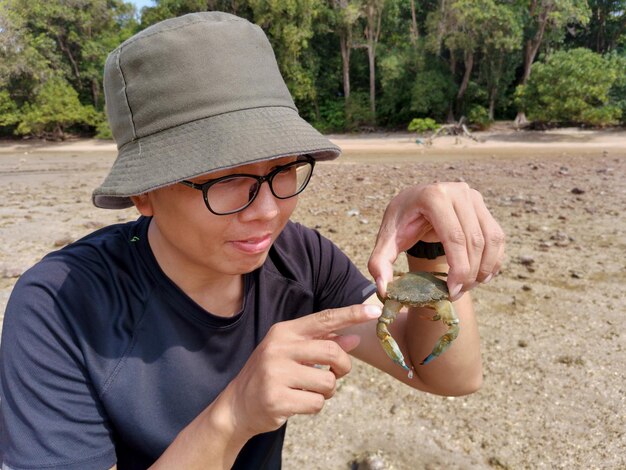 Zdjęcie portret człowieka trzymającego kraba na plaży na tle lasu