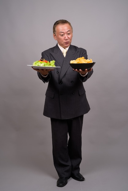 Portret dojrzałego biznesmena azjatyckich przeciw szarej ścianie