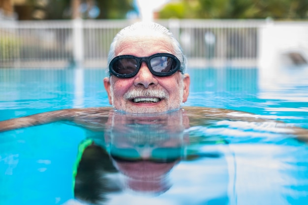 Portret Dojrzałego Mężczyzny Uśmiechającego Się I Patrzącego Na Kamerę W Basenie, Która Bawi Się Sama - Trening I Pływanie Szczęśliwy - Zbliżenie Twarzy Jednego Szczęśliwego Seniora