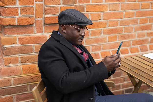 portret dorosłego afrykańskiego mężczyzny z telefonem przy ścianie z cegły