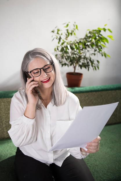 Portret dorosłej kobiety przedsiębiorcy o siwych włosach na stanowisku kierowniczym, ubranej w białą bluzkę i zajętej pracą w biurze