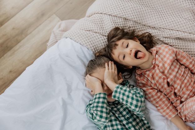 Portret dwóch dziewcząt leżących na łóżku i pozujących na zdjęcie po tym, jak obudziły się i rozciągają się po wielkim śnie