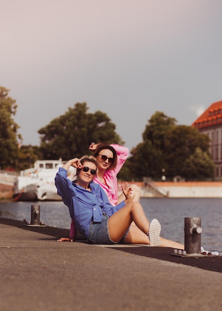 Portret dwóch młodych, pięknych, uśmiechniętych hipster kobiet w modnych letnich ubraniach w kolorze beztroskich kobiet pozujących na tle rzeki Pozytywne modele bawiące się przytulanie