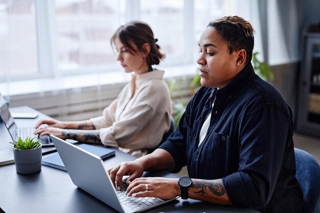 Portret dwóch nowoczesnych kobiet korzystających z laptopów podczas wspólnej pracy w biurze