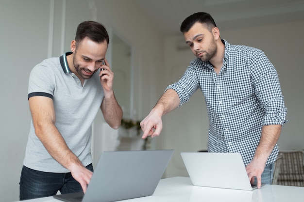 Portret dwóch pewny siebie biznesmen pracuje na laptopie. Jeden mężczyzna rozmawia na smartfonie, gdy inny facet wskazuje palcem na ekranie.