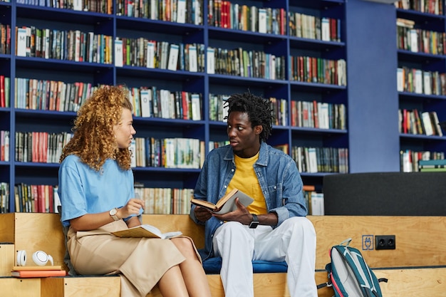 Portret dwóch studentów na czacie w tętniącej życiem bibliotece z niebieską przestrzenią do kopiowania