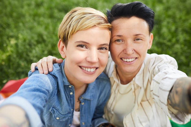 Zdjęcie portret dwóch szczęśliwych lesbijek, uśmiechając się, biorąc selfie portret siedząc na zewnątrz