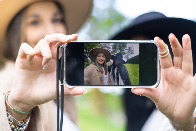 Portret dwóch uśmiechniętych młodych kobiet w kapeluszach robiących selfie w parku