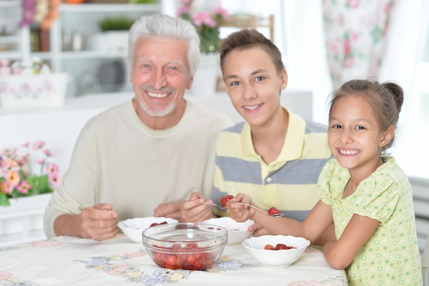 Portret dziadka i wnuków jedzących świeże truskawki w kuchni