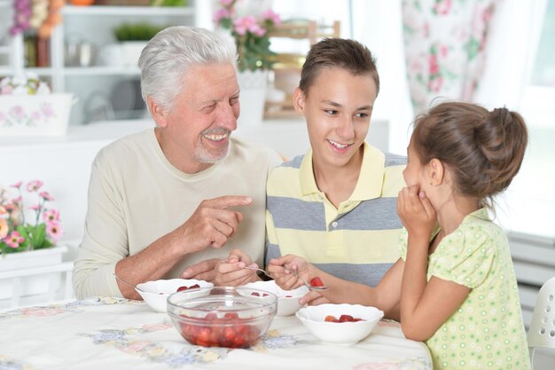 Portret dziadka i wnuków jedzących świeże truskawki w kuchni