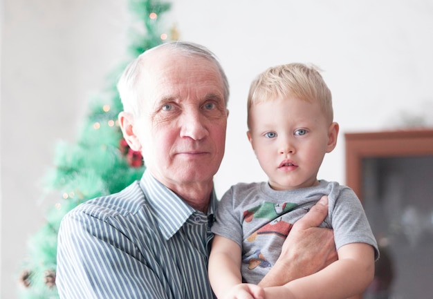 Zdjęcie portret dziadka trzymającego wnuka w ramionach i obaj śmiejący się z choinki