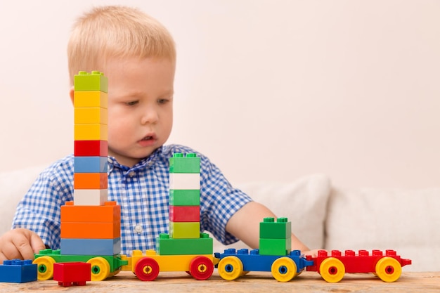Portret dziecka bawiącego się kolorowymi plastikowymi klockami przy stole i budującego pociąg