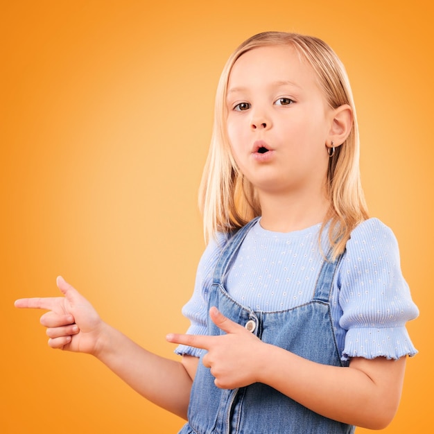 Portret dziecka i dziewczyny z pistoletem w studiu do ogłoszenia reklamowego lub promocji Młody chłopiec na pomarańczowym tle dla gestu ręki wskazującego lub sygnalizującego uwagę na kierunek lub marketing