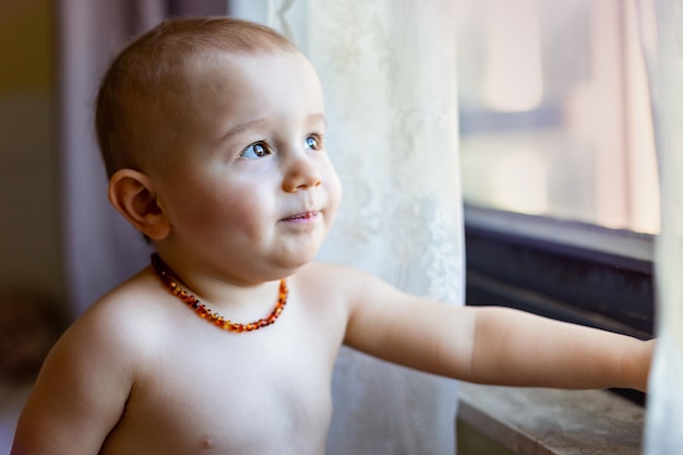 Portret Dziecka Patrzącego Przez Okno Rano Mały Chłopiec W Bursztynowym Naszyjniku Bezbolesna Koncepcja Ząbkowania Naturalny środek Przeciwbólowy