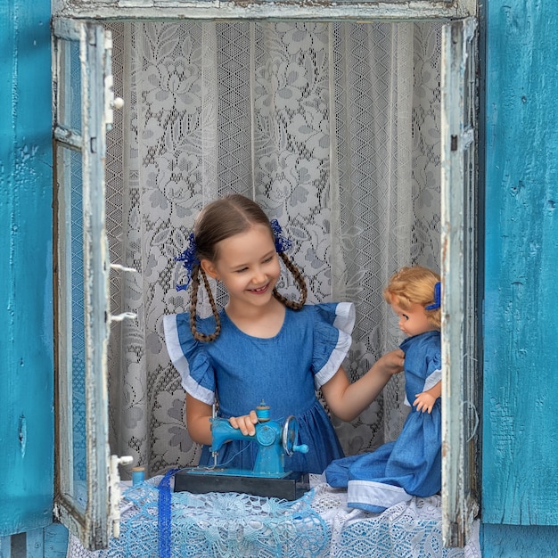 Portret dziewczynki dziecko krawiec szyje robienie ubrań dla lalek na dziecięcej maszynie do szycia w oknie