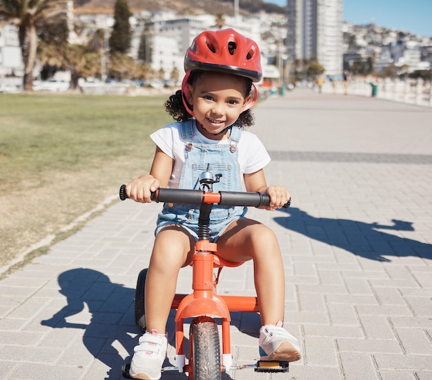 Portret dziewczynki i jazda na rowerze na chodniku ucząca się jeździć na rowerze lub zdrowy rozwój dzieciństwa Szczęśliwe dziecko jeżdżące na trójkołowym rowerze z bezpieczeństwem w kasku i zabawą na świeżym powietrzu w letnim słońcu i Atlancie USA