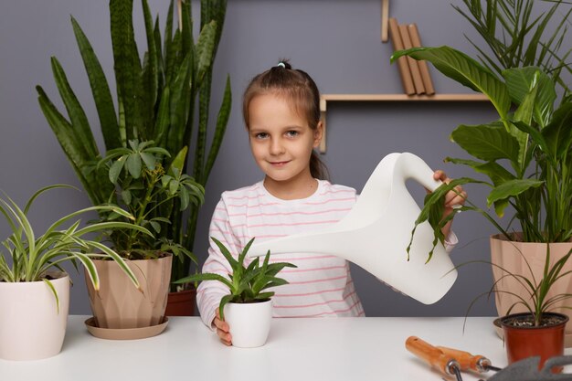 Portret dziewczynki o ciemnych włosach podlewającej rośliny dbającej o kwiaty w pomieszczeniach dziecko pomagające matce kwiaciarni w szklarni trzymającej konewkę patrzącą w kamerę