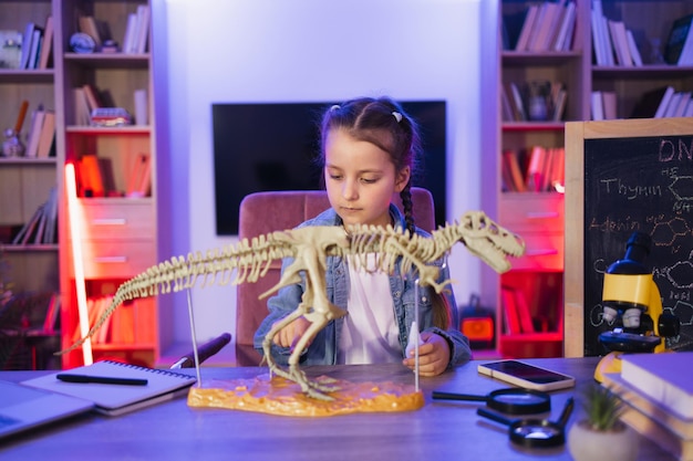 Portret dziewczynki siedzącej przy stole i badającej szkielet dinozaura
