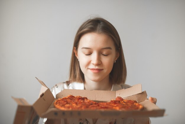 Portret Dziewczynki Trzymającej W Rękach Pudełko Gorącej Pizzy, Z Zamkniętymi Oczami Wącha Zapach Pizzy