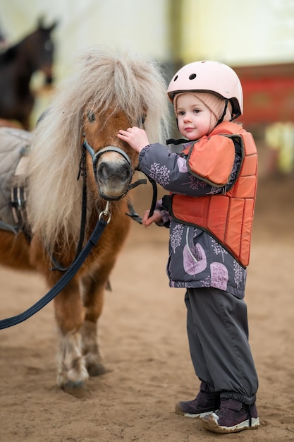 Portret dziewczynki w kurtce ochronnej i hełmie z brązowym kucykiem przed lekcją jazdy konnej
