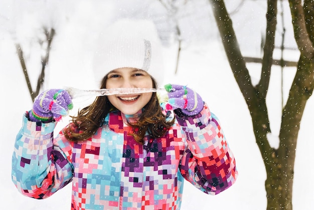 Portret dziewczynki z dużymi soplami podczas zimowego spaceru mała dziewczynka trzyma sopel lodu w dłoni