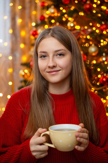 Portret dziewczynki z filiżanką gorącej herbaty lub kawy na tle choinki Świąteczna świąteczna atmosfera