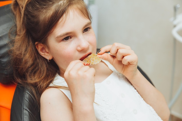 Portret dziewczynki z otwartymi ustami, siedzącej na fotelu dentystycznym, podczas gdy ortodonta trzyma talerz na zębach Dentysta wkłada talerz do ust dziecka